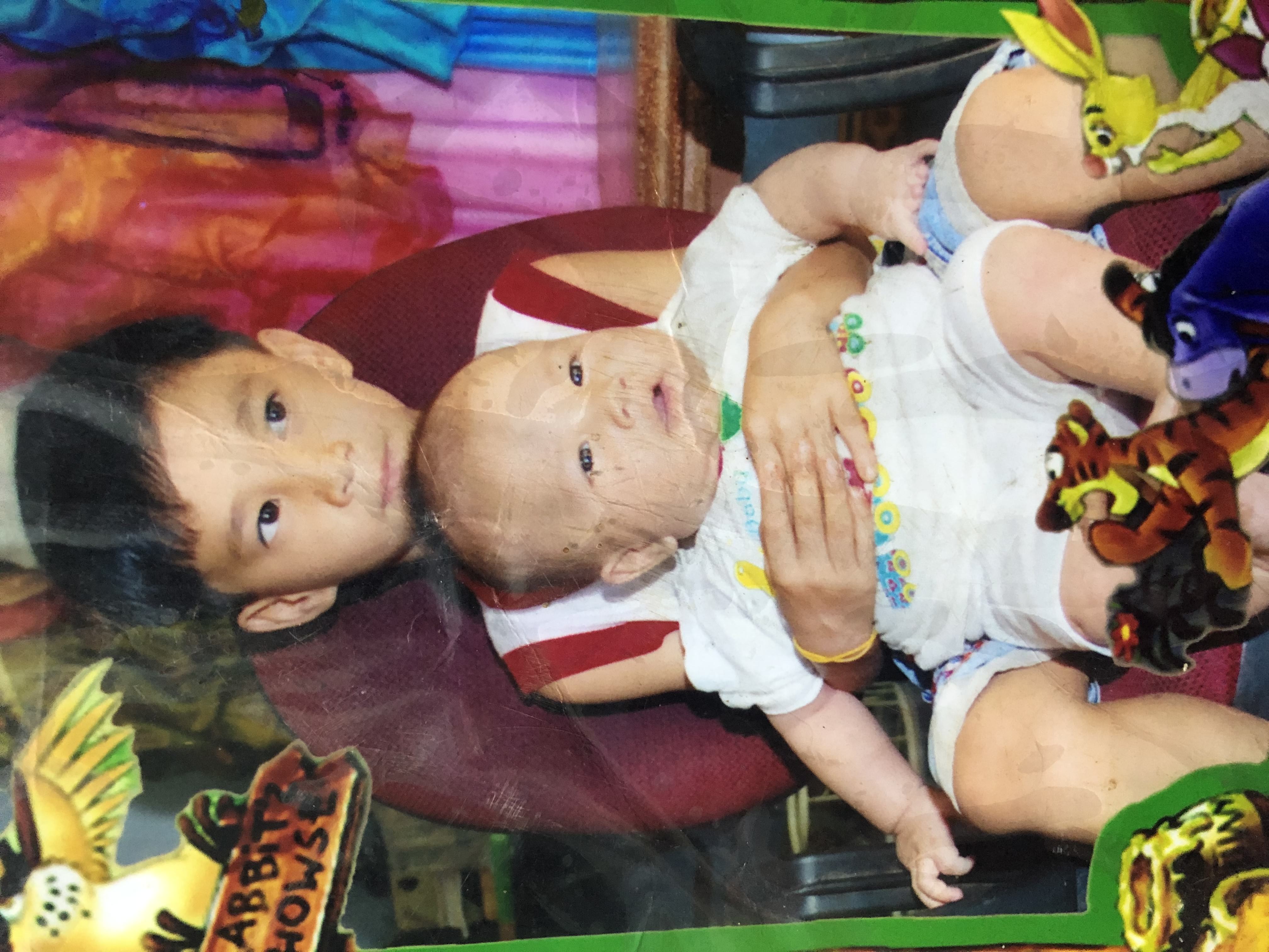 A young boy holding a baby on his lap, with cartoon stickers around the print.